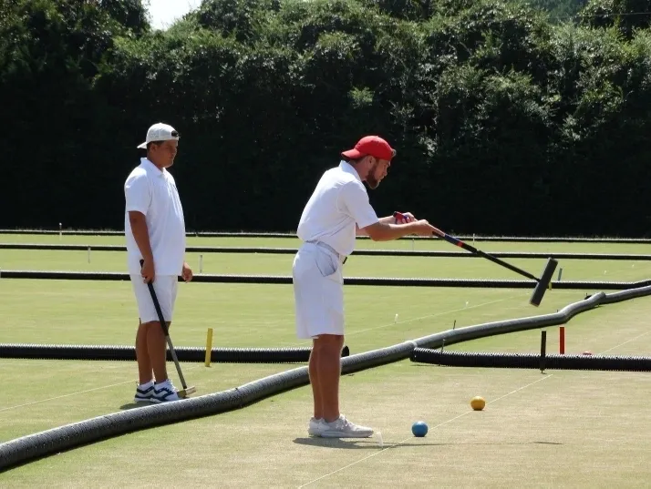 Two men playing a game of croquet on the grass.