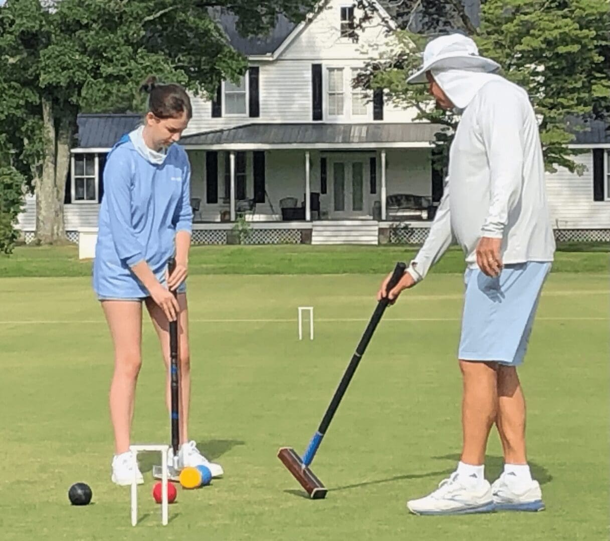Two people playing croquet on a green lawn.